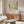 a modern living room with a large abstract painting on the wall, a wooden cabinet, a white sofa, and a glass coffee table.