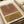 May include: Abstract geometric art print featuring two curved arch designs in terracotta brown and mustard yellow color blocks with black concentric line details, displayed in a light wood frame on a cream-colored surface next to neutral fabric and decorative objects in warm, natural lighting.
