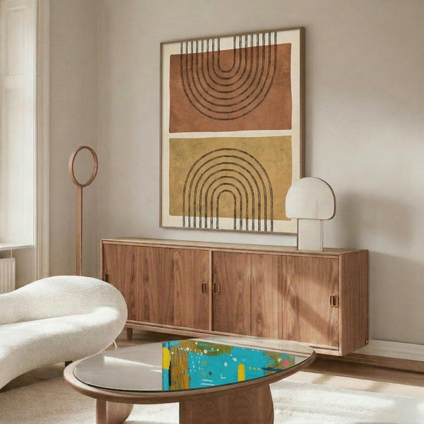 May include: Modern living room featuring a framed abstract print with terracotta and mustard arches on beige wall above wooden credenza. White curved chair, brass floor lamp, marble table lamp, and colorful glass coffee table complete the mid-century styled space with neutral walls and natural lighting.