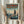 May include: Person in cream sweater holding framed poster print showing astronaut figure standing on rooftop overlooking futuristic city skyline with tall buildings. Artwork features teal and orange color scheme with Japanese text at top and "Lone Pilot of Neo-Tokyo" subtitle. Natural wood frame, person also holding dried pampas grass stems, soft natural lighting from window with white curtains in background.