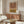 May include: Modern living room interior with walnut credenza displaying the geometric arch poster in warm terracotta and mustard colors. White curved chair, glass coffee table with wooden base, brass floor lamp, and dome table lamp create a mid-century modern aesthetic. The framed artwork features concentric semicircular arches in earth tones against cream background, complementing the neutral wall and natural lighting from nearby window.