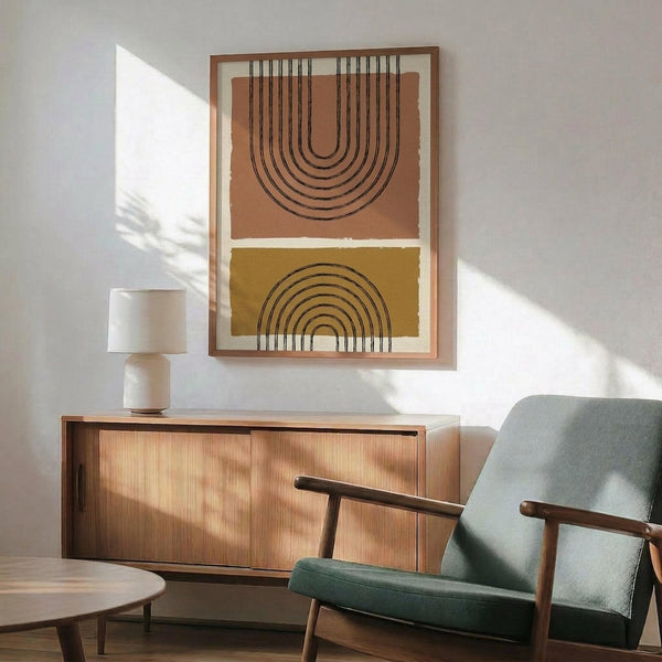 May include: Abstract geometric wall art featuring two arched designs - an upside-down arch in terracotta orange and a rainbow arch in mustard yellow, both with black concentric lines on cream background. Wooden frame hangs above mid-century modern furniture including walnut credenza, sage green upholstered armchair with wooden frame, small round coffee table, and white ceramic table lamp. Warm sunlight streams across white walls.