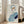 May include: Framed abstract portrait artwork leaning against white wall next to beige upholstered chair. The minimalist illustration features a stylized face with blue hair, orange and pink facial features, single visible eye, and geometric blue and navy clothing shapes. Light wooden frame on hardwood floors in bright, airy room with large windows.