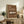 May include: Framed brown poster featuring white vintage Porsche 911 with "PORSCHE 911 CLASSIC 1964" text, displayed on rustic wooden console with books, ceramic vase, and fern plant in cozy living room setting with beige armchair and neutral walls