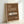 May include: Framed vintage-style poster with brown background featuring white Porsche 911 sports car illustration, cream typography reading "911 CLASSIC" and "1964", displayed in light wood frame leaning against white wall corner with natural lighting casting soft shadows.