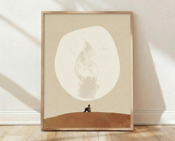 May include: Framed minimalist poster print featuring a small silhouetted figure sitting on an orange-brown curved landscape beneath a large white crescent moon on a beige background. Light wooden frame sits on wooden floor against white wall with soft natural lighting and shadows.