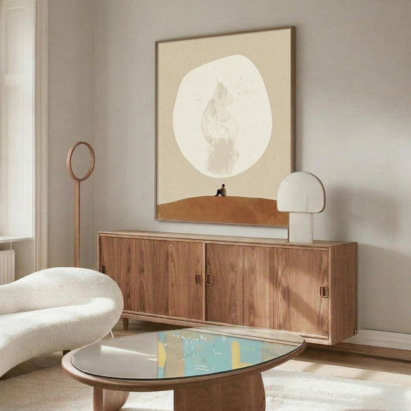 May include: Framed beige and white abstract poster with oval shape and subtle figure silhouette, displayed above walnut wood sideboard in modern living room. White mushroom table lamp, curved cream chair, oval glass coffee table with colorful abstract surface, and tall brass mirror on stand complete the neutral-toned Scandinavian-style interior scene.