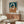 May include: Abstract art print with interlocking oval rings in terracotta orange, navy blue, and cream colors, displayed in thin wooden frame above mid-century walnut credenza. Modern living room setting features white upholstered chair, glass-top coffee table, and brass floor lamp with circular mirror detail.