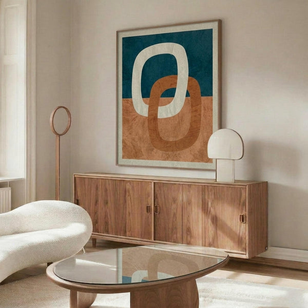 May include: Abstract art print with interlocking oval rings in terracotta orange, navy blue, and cream colors, displayed in thin wooden frame above mid-century walnut credenza. Modern living room setting features white upholstered chair, glass-top coffee table, and brass floor lamp with circular mirror detail.