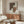 May include: Abstract geometric art print with earthy brown, cream, and terracotta shapes featuring dotted textures, displayed in thin wooden frame above mid-century walnut credenza. Modern living room setting with white curved chair, round glass coffee table, and warm natural lighting creating soft shadows on neutral walls.