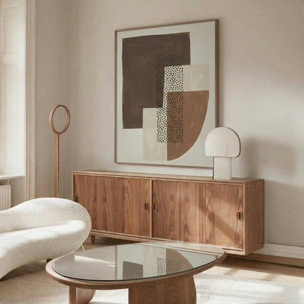 May include: Abstract geometric art print with earthy brown, cream, and terracotta shapes featuring dotted textures, displayed in thin wooden frame above mid-century walnut credenza. Modern living room setting with white curved chair, round glass coffee table, and warm natural lighting creating soft shadows on neutral walls.