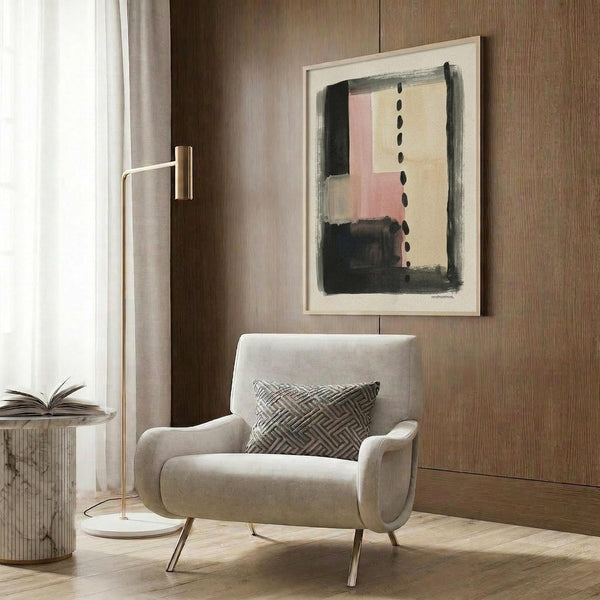 May include: Abstract art print with muted pink, cream, and dark brushstrokes plus vertical black dots, displayed in light wood frame on textured wood wall above beige upholstered chair with geometric pillow, brass floor lamp and marble side table with open book nearby