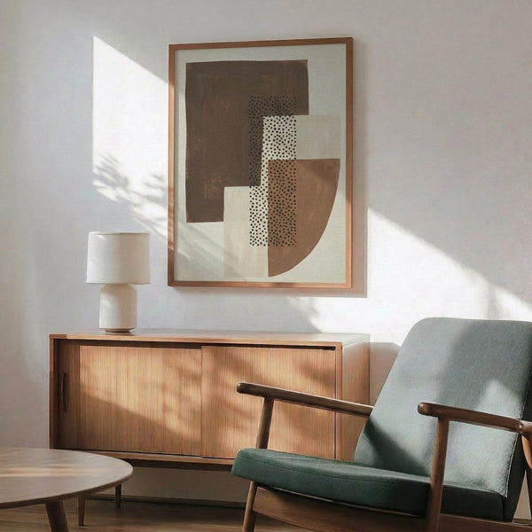 May include: Abstract geometric poster with brown, beige, and dotted pattern shapes displayed in wooden frame above mid-century modern credenza. Scene shows mint green upholstered chair with wooden arms, white ceramic table lamp, and natural sunlight casting shadows on white wall in contemporary living room setting.