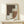 May include: Abstract geometric art print in natural wood frame leaning against white wall on light wooden surface. Artwork features overlapping brown, cream, and dotted pattern shapes in earthy tones. Small wrapped gift with evergreen sprig sits beside frame. Minimalist Scandinavian-style room setting with soft natural lighting and neutral color palette.