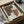 May include: Abstract geometric art print in earth tones featuring overlapping curved shapes in brown and tan with dotted stippled texture pattern. Black frame with white mat sitting in cardboard shipping box with wooden dowels and protective tissue paper wrapping.