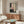 May include: Abstract artwork in wood frame hanging above mid-century walnut credenza, featuring geometric blocks in black, pink, cream and gray with vertical dotted line. Modern living room setting with white curved chair, oval glass coffee table, and minimalist decor against neutral walls.