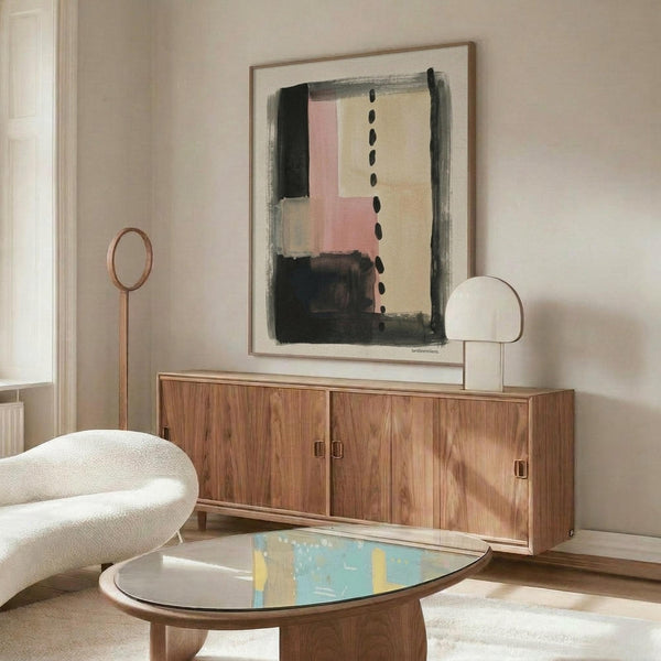 May include: Abstract artwork in wood frame hanging above mid-century walnut credenza, featuring geometric blocks in black, pink, cream and gray with vertical dotted line. Modern living room setting with white curved chair, oval glass coffee table, and minimalist decor against neutral walls.