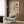 May include: Modern abstract poster with overlapping geometric shapes in warm terracotta, sage green, and cream tones, displayed in light wood frame on wood-paneled wall. Styled with beige upholstered armchair featuring geometric pillow, brass floor lamp, and dark round side table with open book in contemporary living room setting.