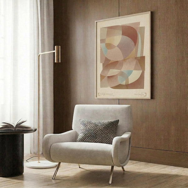May include: Modern abstract poster with overlapping geometric shapes in warm terracotta, sage green, and cream tones, displayed in light wood frame on wood-paneled wall. Styled with beige upholstered armchair featuring geometric pillow, brass floor lamp, and dark round side table with open book in contemporary living room setting.