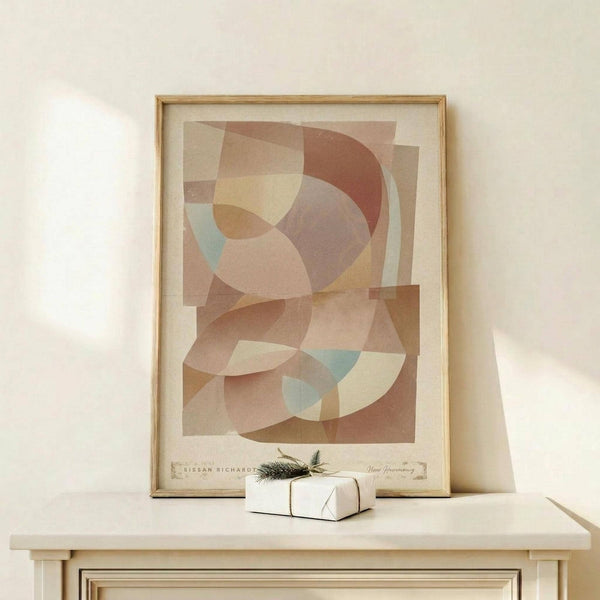 May include: Abstract geometric art print in warm earth tones with overlapping circular and curved shapes in terracotta, sage green, cream, and dusty pink. Displayed in thin natural wood frame on light wooden console table beside small white wrapped gift with evergreen sprig. Soft natural lighting creates gentle shadows on cream wall.