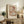 May include: Abstract geometric art print in muted earth tones featuring overlapping circular and angular shapes in soft browns, peaches, and dusty blue, displayed in light wood frame on rustic wooden sideboard alongside fern plant, ceramic vase, and leather chair in warm-lit living room setting.