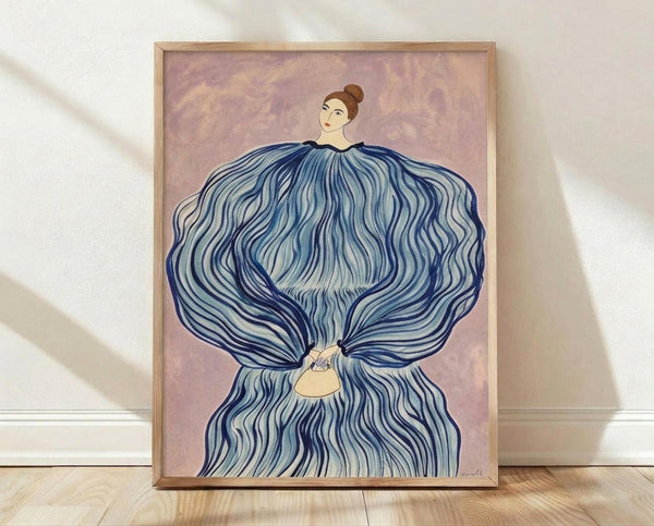 May include: Framed art print leaning against white wall on wooden floor. Artwork shows woman with brown hair bun wearing flowing blue dress or fabric that billows dramatically around her body. Purple-pink cloudy background. Simple wooden frame. Soft natural lighting creates gentle shadows on textured white wall.