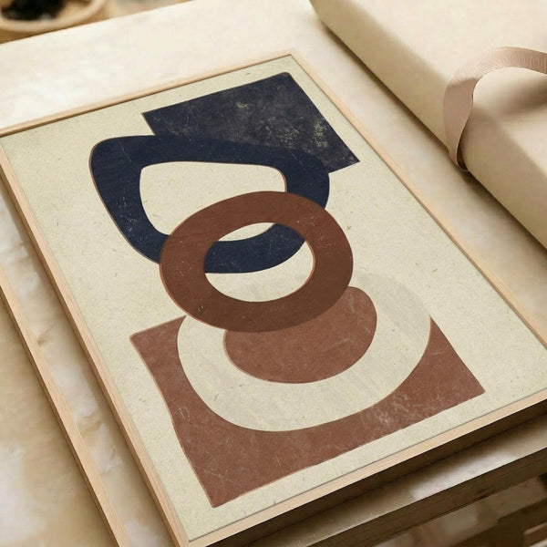 Abstract geometric print with interlocking curved and angular shapes in navy blue and rust brown on cream background. The weathered, textured design shows vintage-style distressing. Print lies flat on light wooden surface next to rolled kraft paper, creating an artistic workspace scene.