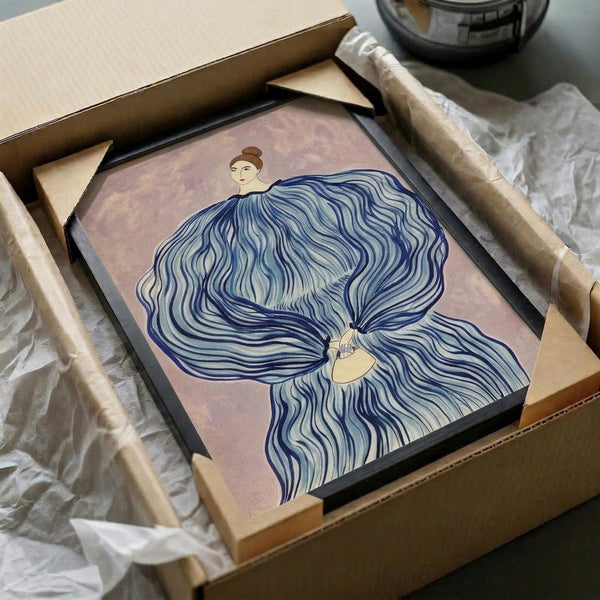May include: Framed artwork in black frame being unpacked from cardboard box with tissue paper. The poster shows two figures with flowing blue hair against a pink background in an Art Deco style. Wooden frame corners and protective packaging materials visible around the square print.