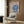 May include: Framed art print featuring a woman in an elaborate blue flowing gown with dramatic fabric draping, displayed above a beige upholstered armchair with geometric pillow in a modern room setting with wood paneled walls, gold floor lamp, and dark round side table with open book.