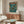 May include: Framed poster with Japanese text and Neo Tokyo title, showing illustrated figure with mech robot on rainy city street with neon signs and tall buildings. Teal and orange color scheme. Displayed above mid-century modern walnut credenza with sliding doors in minimalist living room with white curved chair, round glass coffee table, and modern floor lamp.