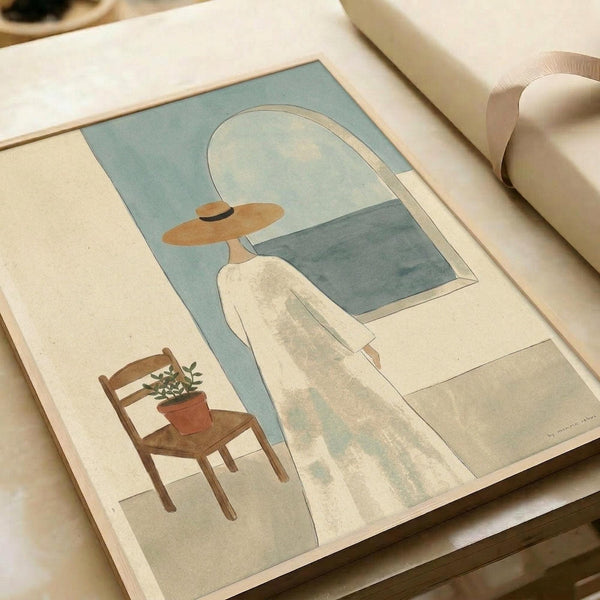 May include: Minimalist art print displayed on light wooden surface showing a figure in white dress and wide-brimmed tan hat standing before an arched window overlooking the sea, with a wooden chair holding a potted plant nearby. The artwork features soft muted tones of sage green, cream, and dusty blue in a contemporary illustration style.