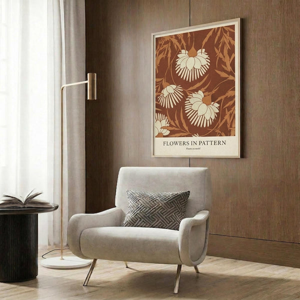 May include: Beige armchair with geometric patterned pillow positioned next to brass floor lamp and dark round side table with open book. Behind chair, wood-paneled wall displays framed botanical poster featuring brown and cream floral pattern with leaves and stylized flowers. Natural light filters through white curtains onto wooden flooring.
