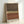 May include: Framed abstract art print leaning against white wall, featuring horizontal bands in brown, tan, rust orange, and cream with scattered black dots creating a stippled pattern across the center. Light wood frame, textured painted surfaces with subtle shimmer, positioned on light surface casting soft shadow.