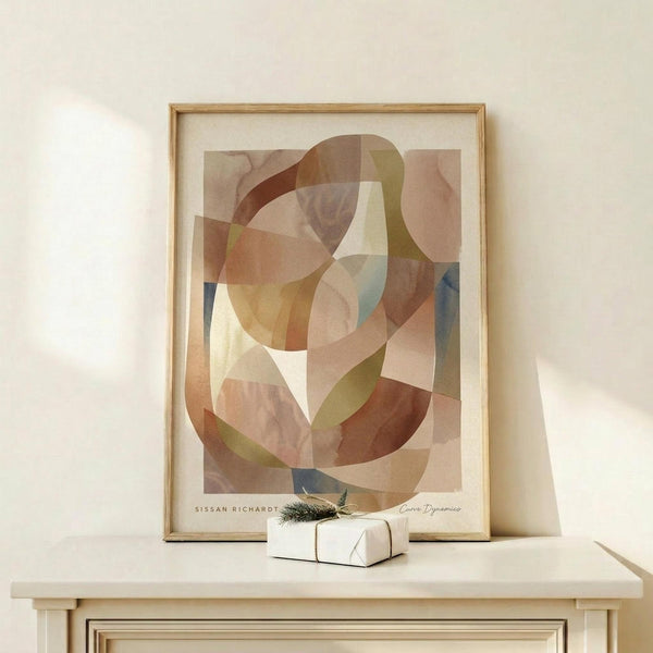May include: Abstract art print in light wooden frame displaying overlapping curved shapes in warm earth tones - browns, beiges, soft greens and muted blues with transparent layering effects. Framed artwork sits on pale wooden surface next to small white wrapped gift with green sprig, against cream colored wall with soft natural lighting.
