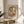 May include: Abstract art print with overlapping curved shapes in warm earth tones including terracotta, sage green, cream, and muted blue, displayed in a thin wood frame on a round wooden side table next to a beige upholstered chair, with soft natural lighting and plant shadows visible on white walls.