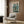 May include: Framed poster with Japanese text and mech robot artwork displayed on wood paneled wall above beige armchair with geometric patterned pillow. Modern reading corner with brass floor lamp and dark round side table holding open book. Warm neutral tones throughout minimalist interior space.