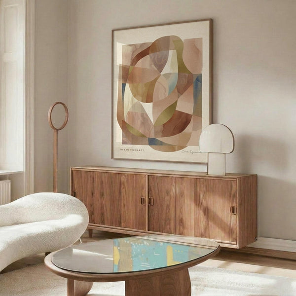 May include: Abstract art print with overlapping curved shapes in warm earth tones - browns, oranges, teals, and cream - displayed in thin wooden frame above mid-century walnut credenza. Modern living room setting features white sculptural chair, oval glass coffee table, and contemporary brass floor lamp. Soft natural lighting creates peaceful, minimalist atmosphere with neutral beige walls.