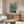 May include: Framed poster with Japanese text and robotic mecha figure standing in futuristic cityscape with lightning and rain, displayed above wooden credenza in modern living room with white curved chair, glass coffee table, and minimalist decor in neutral tones.