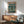 May include: Framed poster with Japanese text and cyberpunk robot mech standing in futuristic city with lightning and rain, displayed above wooden sideboard with white table lamp in modern living room setting with mint green mid-century armchair and round coffee table