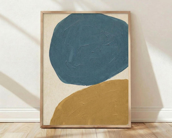 May include: Framed abstract art print featuring two large organic shapes - a teal blue circular form above and a golden mustard curved shape below - painted on cream background. Visible brushstrokes and texture throughout. Natural wood frame leaning against white wall on light wooden floor with soft shadows.