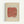 Abstract artwork in light wood frame featuring a coral-red brushstroke shape with olive green dots scattered across it, set against pale blue and cream vertical stripes on textured cream background, mounted on white wall