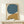 May include: Abstract artwork in wooden frame featuring large teal blue circle and golden mustard curved shape on cream background, displayed on light wood console table with small wrapped gift decorated with evergreen sprig against white wall