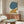 May include: Abstract poster with large teal blue circle and golden yellow curved shape on cream background, displayed in thin wooden frame above mid-century walnut credenza in modern living room with white sculptural chair, brass floor lamp, and oval glass coffee table