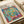 May include: Matisse-style art print showing colorful interior scene with open window, tropical plants, and teacup on table. Vibrant blues, greens, oranges, and pinks in fauve painting style. Print displayed on cream-colored surface with soft natural lighting and neutral background setting.