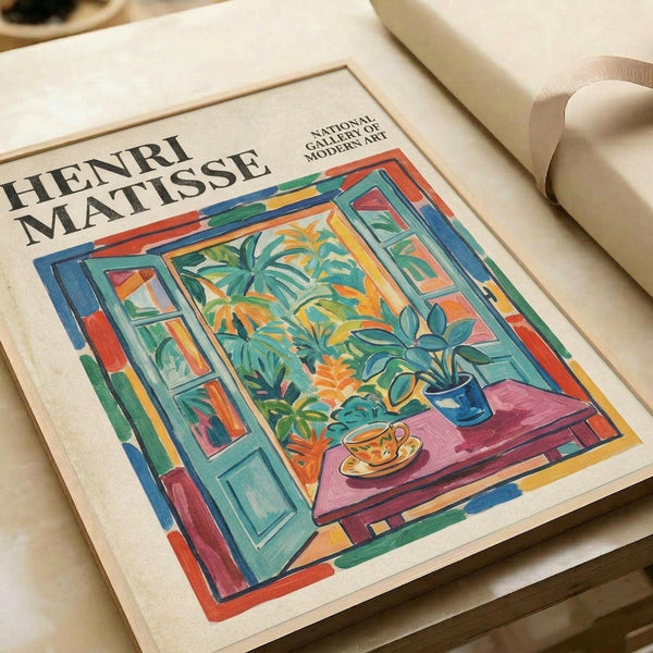 May include: Matisse-style art print showing colorful interior scene with open window, tropical plants, and teacup on table. Vibrant blues, greens, oranges, and pinks in fauve painting style. Print displayed on cream-colored surface with soft natural lighting and neutral background setting.