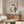 May include: Framed vintage Japanese frog artwork hanging above a walnut credenza in a modern living room. The print features a large green and cream colored frog in traditional woodblock style with red Japanese characters. Room has white walls, curved white chair, oval glass coffee table, and white mushroom lamp on the sideboard.