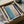 May include: Abstract art print with soft blue and coral pink watercolor washes separated by bold navy blue geometric lines, displayed in black frame inside cardboard shipping box with white tissue paper and bubble wrap protective packaging