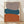 May include: Framed abstract geometric art print with three stacked organic shapes in muted brown, teal blue, and rust orange against cream background, displayed in light wood frame on wooden floor against white textured wall with natural lighting creating soft shadows.
