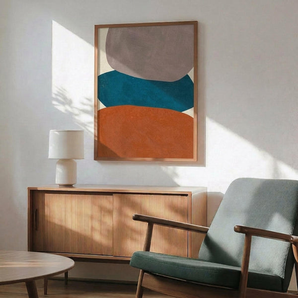 May include: Abstract geometric poster with organic rounded shapes in terracotta orange, teal blue, and taupe gray on cream background, displayed in thin wood frame above mid-century modern sideboard. Scene shows sage green upholstered armchair with wooden arms, small table lamp, and round coffee table in minimalist living room with white walls and natural sunlight casting shadows.