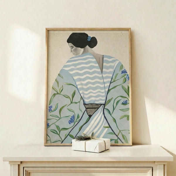 May include: Framed art print displayed on light wood console table with small wrapped gift box. Print shows woman in profile wearing blue and white striped kimono with green floral botanical pattern and small blue flowers. Figure has black hair with blue hair ornament against cream background. Natural wood frame in bright, minimalist room setting.